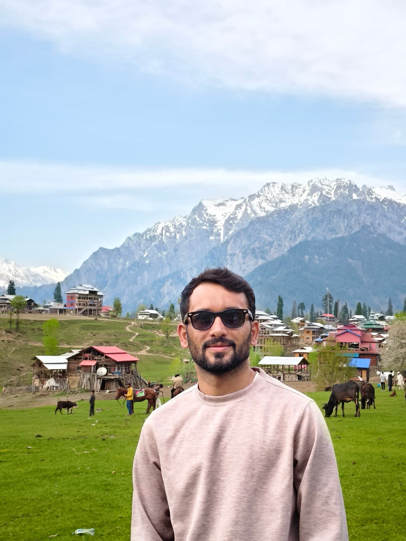 A working village pasture in the shadow of the range — horses, cattle, and wood-shingle roofs everywhere.